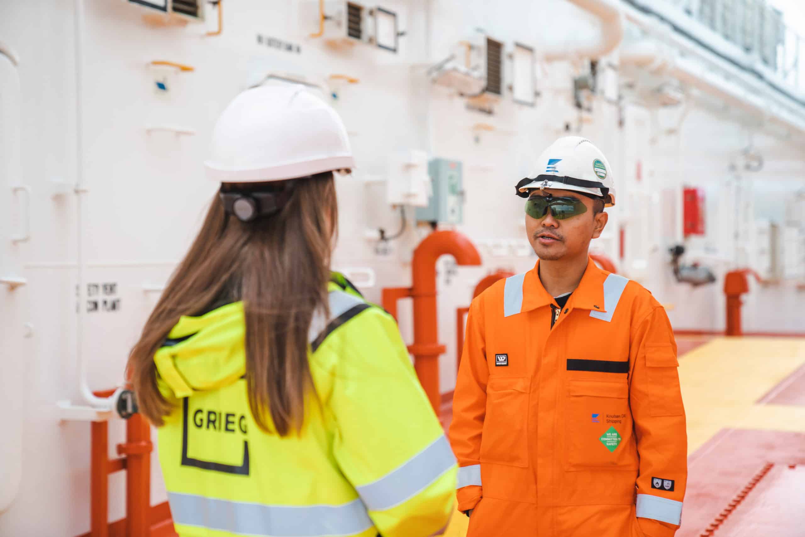 Grieg colleagues in organge and yellow uniform having a chat on the deck of a ship.